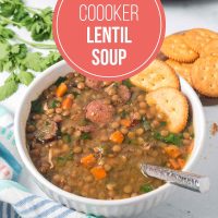 Bowl of lentil soup with kielbasa, spinach, carrots, onion, and green pepper garnished with crackers with text Slow Cooker Lentil Soup.