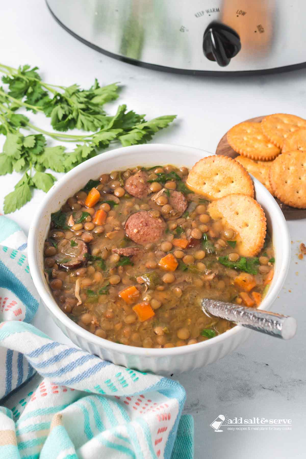 Bowl of lentil soup with kielbasa, spinach, carrots, onion, and green pepper garnished with crackers.
