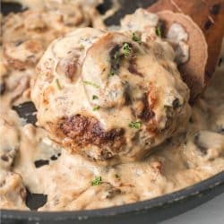 Salisbury Steak patty in mushroom cream sauce in a black pan with a serving spoon.