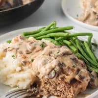 White plate with a Salisbury Steak patty and mashed potatoes smothered in mushroom cream sauce with green beans and text Easy Mushroom Salisbury Steak.