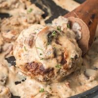 Salisbury Steak in a mushroom cream sauce in a black pan with a wooden spoon.
