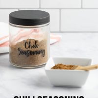 Jar of homemade chili seasoning beside a dish of the seasoning with a small wooden spoon and text chili seasoning - homemade gift mix