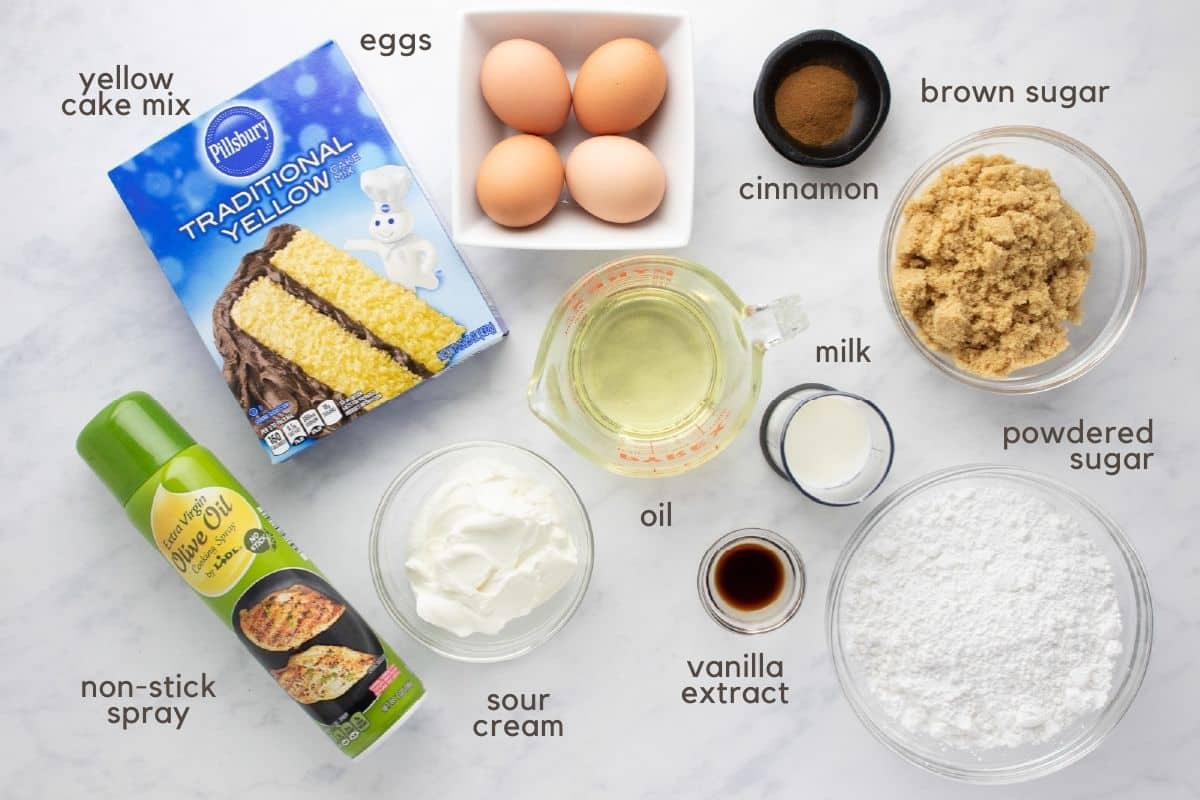 Ingredients needed to make honey bun cake: yellow cake mix, eggs, cooking oil, sour cream, cinnamon, brown sugar, powdered sugar, milk, vanilla, and non-stick baking spray.