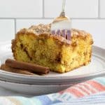 Slice of Honey Bun Cake on a plate showing the cinnamon swirl in the middle and vanilla glaze on top with a fork stuck in the top of the cake.