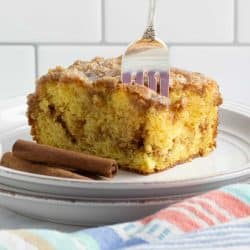 Slice of Honey Bun Cake on a plate showing the cinnamon swirl in the middle and vanilla glaze on top with a fork stuck in the top of the cake.