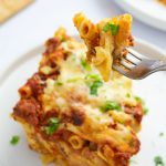 Forkful of Cheesy Meatless Baked Ziti garnished with fresh parsley held above a serving of the ziti on a plate.