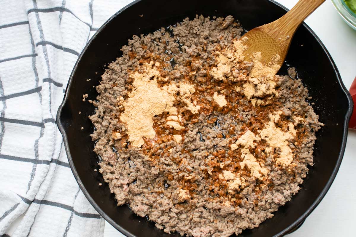 Overhead shot of ground beef in a cast iron skillet with taco seasoning on top.