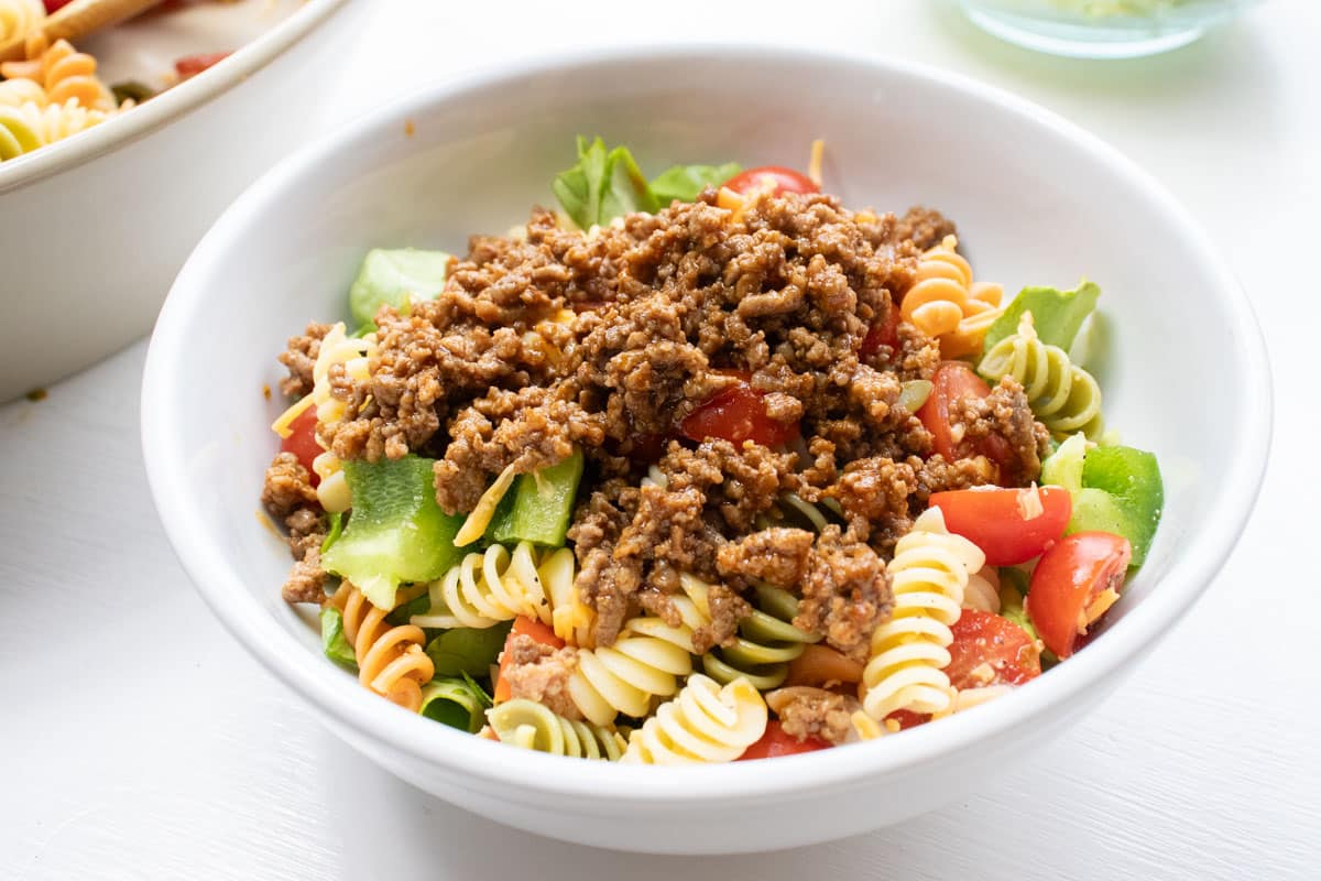 Bowl of seasoned ground beef, spiral pasta, lettuce, and halved tomatoes.