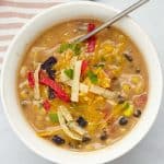 A bowl of chicken enchilada soup garnished with shredded cheddar cheese, cilantro, and tortilla strips.