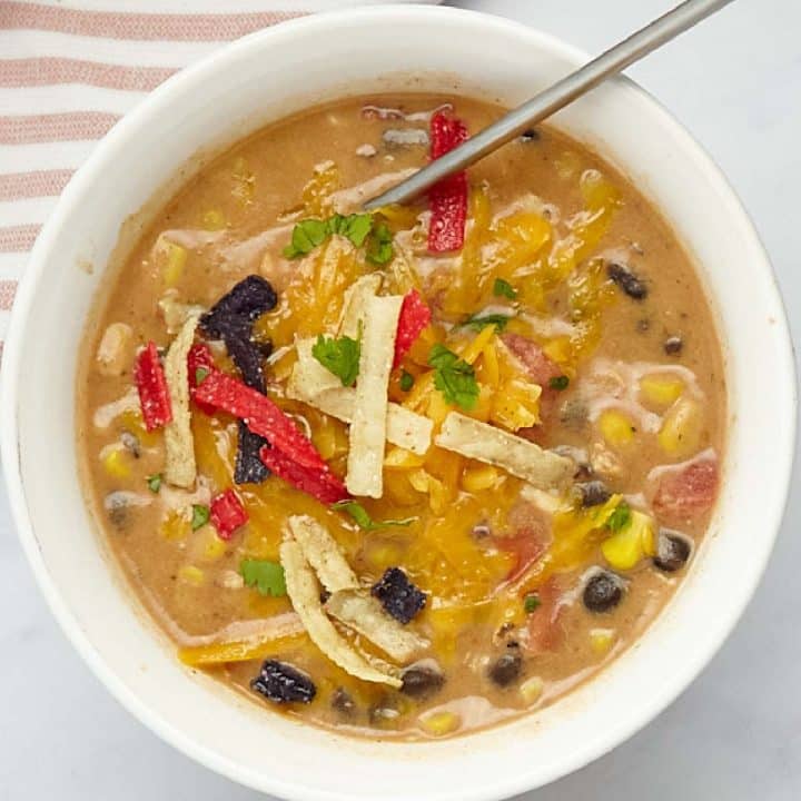 A bowl of chicken enchilada soup garnished with shredded cheddar cheese, cilantro, and tortilla strips.