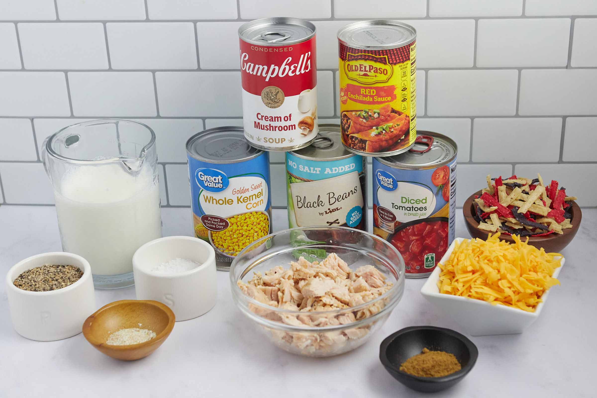 Ingredients for soup: milk, canned corn, canned black beans, cream of mushroom soup, red enchilada sauce, can of diced tomatoes, chopped rotisserie chicken, salt, pepper, cumin, garlic salt, shredded cheddar cheese, and tortilla strips.