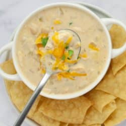 A bowl of creamy white chicken chili garnished with cheddar cheese and cilantro and served with chips.