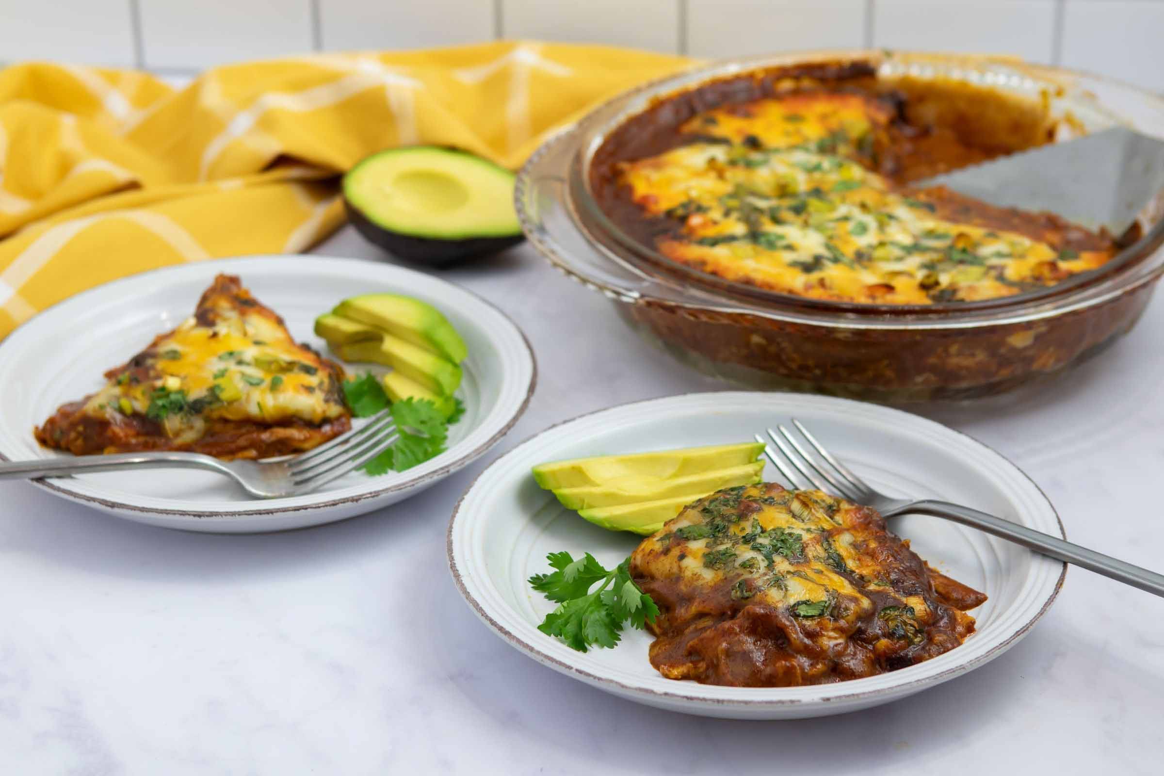 Two plates with chicken enchilada bake garnished with sliced avocado.