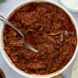 Bowl full of seasoned beef burrito filling with a fork.