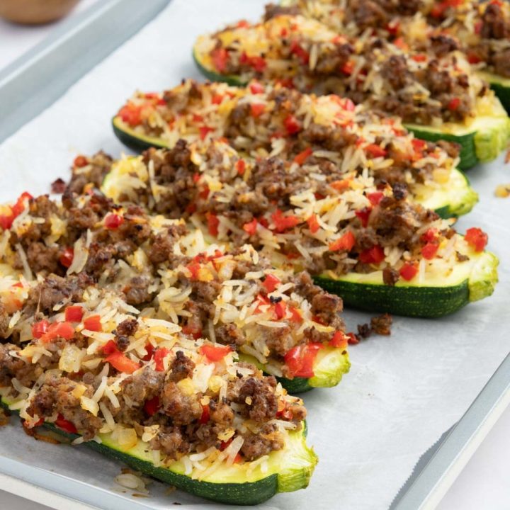 Baked zucchini stuffed with a rice, ground beef, and vegetable mixture on a baking sheet lined with parchment paper.