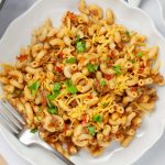 Plate of macaroni, beef, and tomatoes in a cheesy sauce garnished with cilantro and grated cheddar cheese