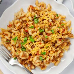 Plate of macaroni, beef, and tomatoes in a cheesy sauce garnished with cilantro and grated cheddar cheese