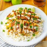 Chicken breast over rice drizzled with white sauce and garnished with green onions beside a glass of iced tea and two limes.