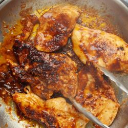 Boneless, skinless chicken breasts in a rich chili sauce being sautéed in a skillet.