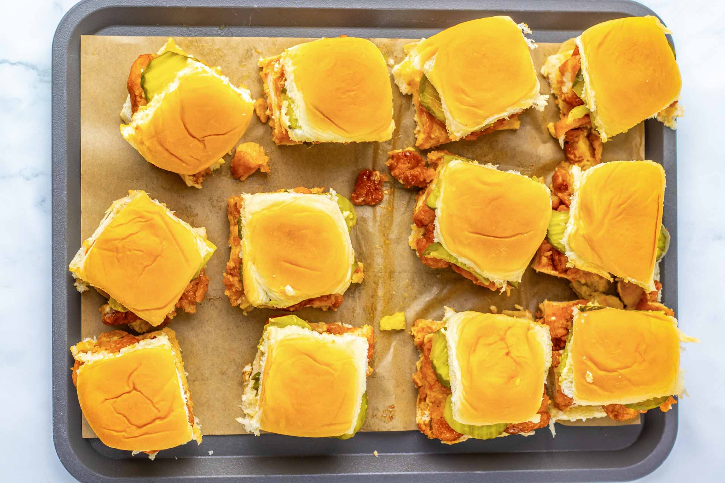Overhead view of a dozen hot honey chicken sliders on a baking sheet.