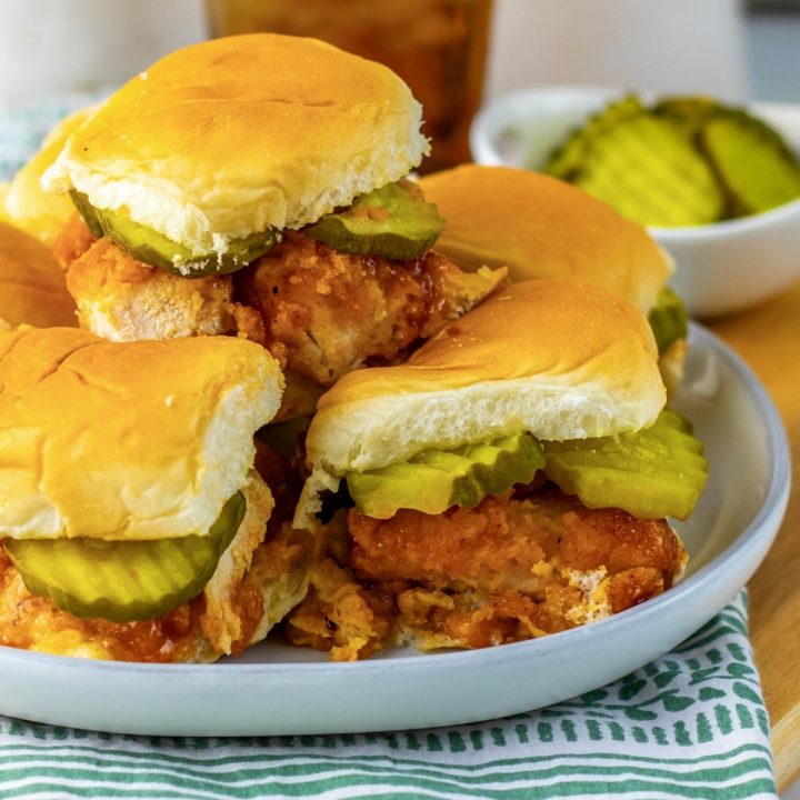 A pile of hot honey chicken sliders with pickles on a plate.