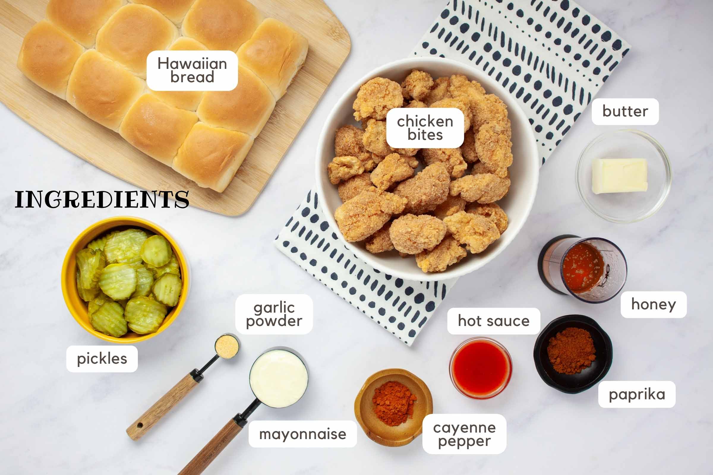 Ingredients on a counter: Frozen chicken bites, butter, honey, paprika, hot sauce, cayenne pepper, mayonnaise, garlic powder, pickles, and Hawaiian bread.