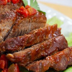 Sliced pot roast with diced tomatoes on top and a red sauce.