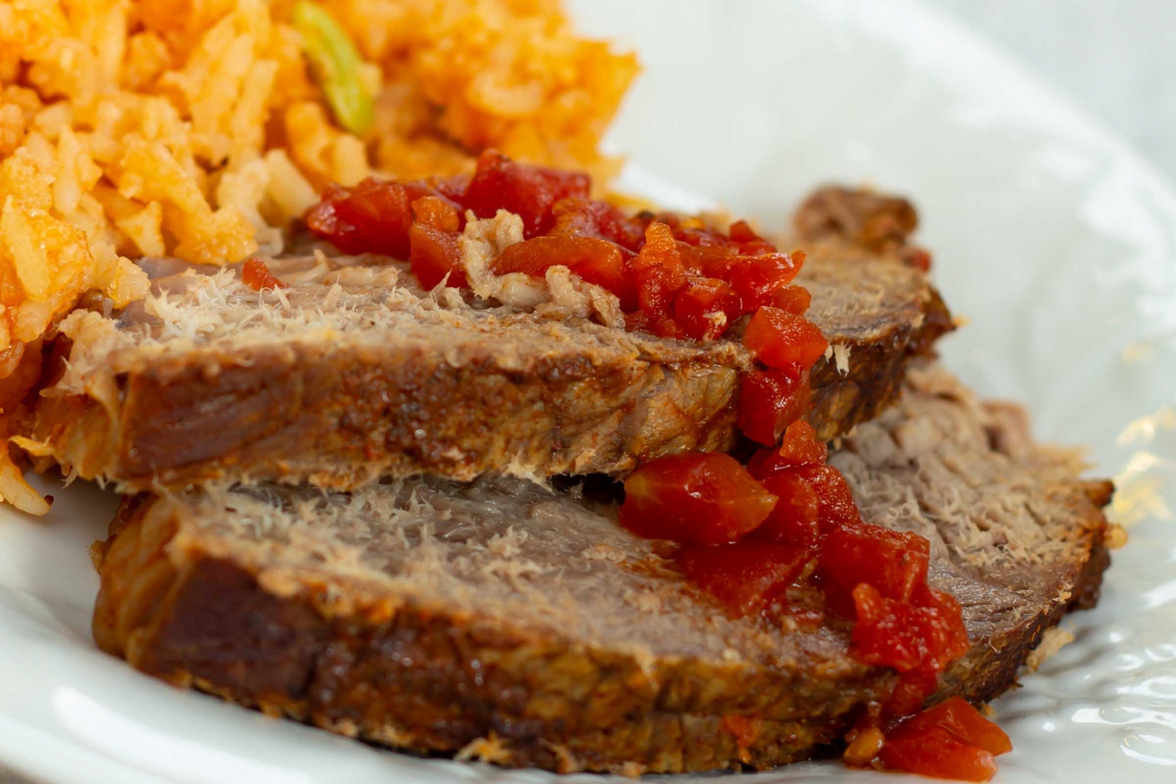 Slices of pot roast on a plate beside Mexican rice.