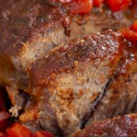 Sliced pot roast with diced tomatoes on top and a red sauce with text Crockpot Mexican Pot Roast - tender & delicious.