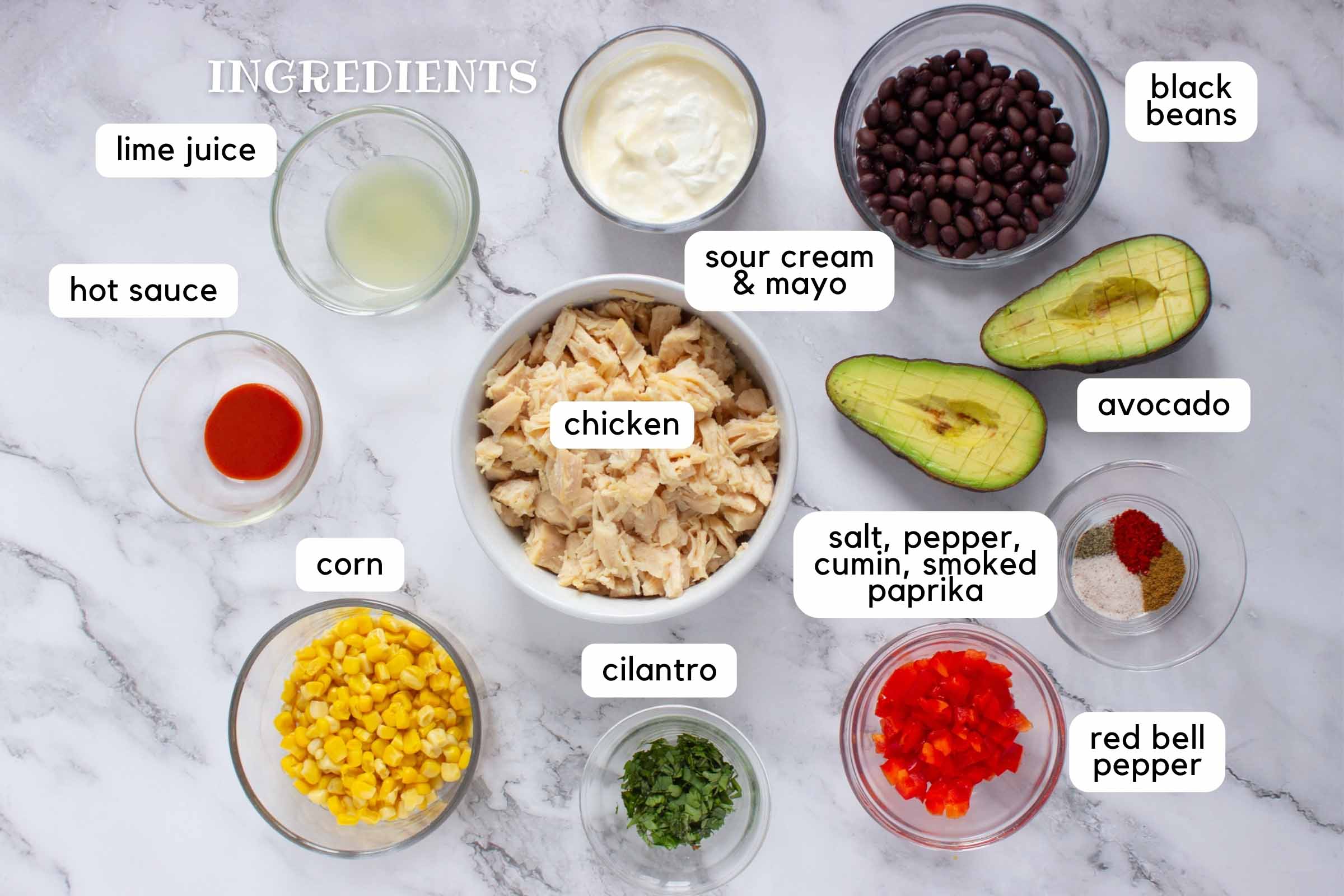 Labeled ingredients on a counter: Chicken, corn, cilantro, salt, pepper, cumin, smoked paprika, red bell pepper, avocado, black beans, sour cream & mayo, lime juice, and hot sauce.