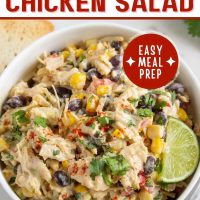 Bowl of chicken salad with corn, black beans, avocado, and red bell pepper in a creamy dressing garnished with a lime wedge and sprinkled with paprika with text Southwest Chicken Salad - easy meal prep.