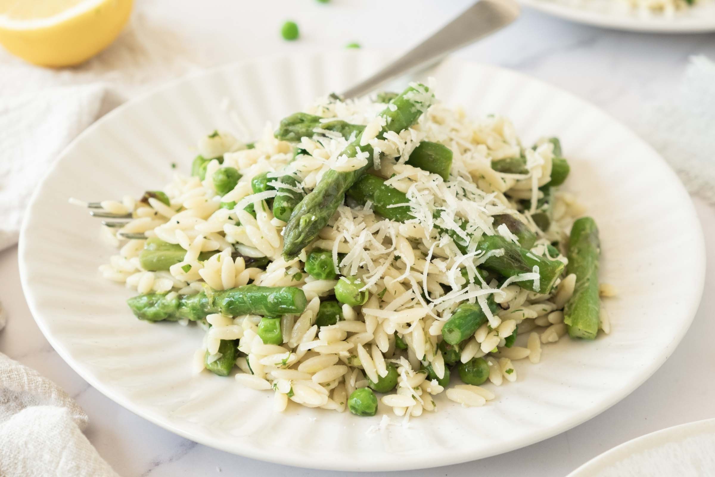 Plate of orzo with peas and asparagus garnished with grated Parmesan cheese.