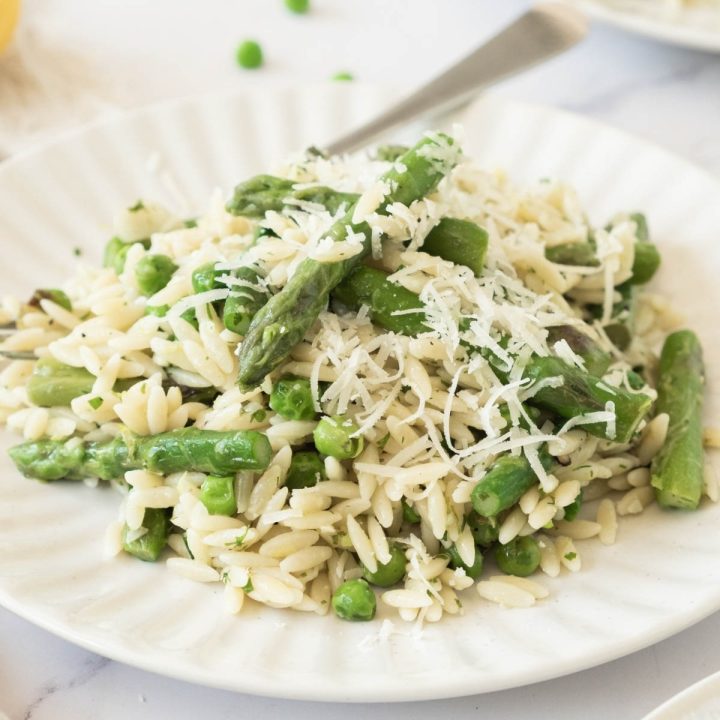 Plate of orzo with peas and asparagus garnished with grated Parmesan cheese.