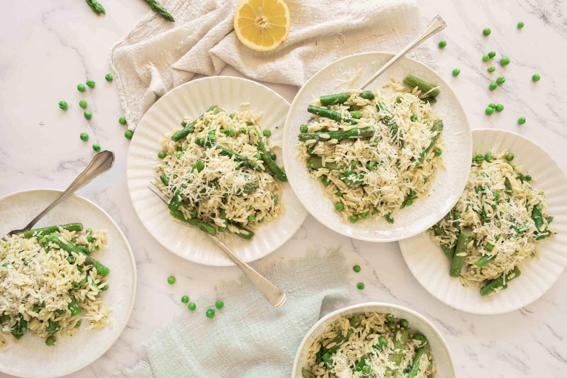 Plates of orzo with peas and asparagus on a counter beside half a lemon.