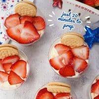 Red, white, and blue parfaits in plastic cups topped with sliced strawberries and a sandwich cookie with text Fourth of July Dessert Cups - just 20 minutes to prep.