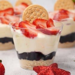 Red, white, and blue parfaits in plastic cups topped with sliced strawberries and a sandwich cookie.