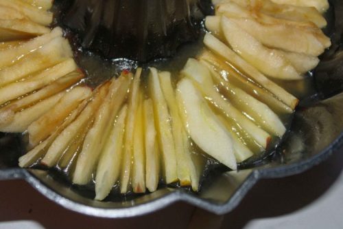 Peeled and sliced apples placed in a butter brown sugar mixture in a bundt pan.