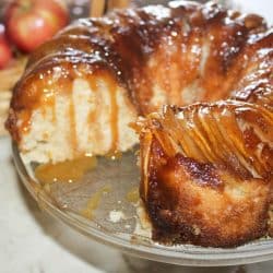 Apple upside down bundt cake with a slice removed and caramel sauce dripping down the sides.