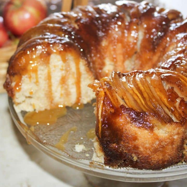 Apple upside down bundt cake with a slice removed and caramel sauce dripping down the sides.