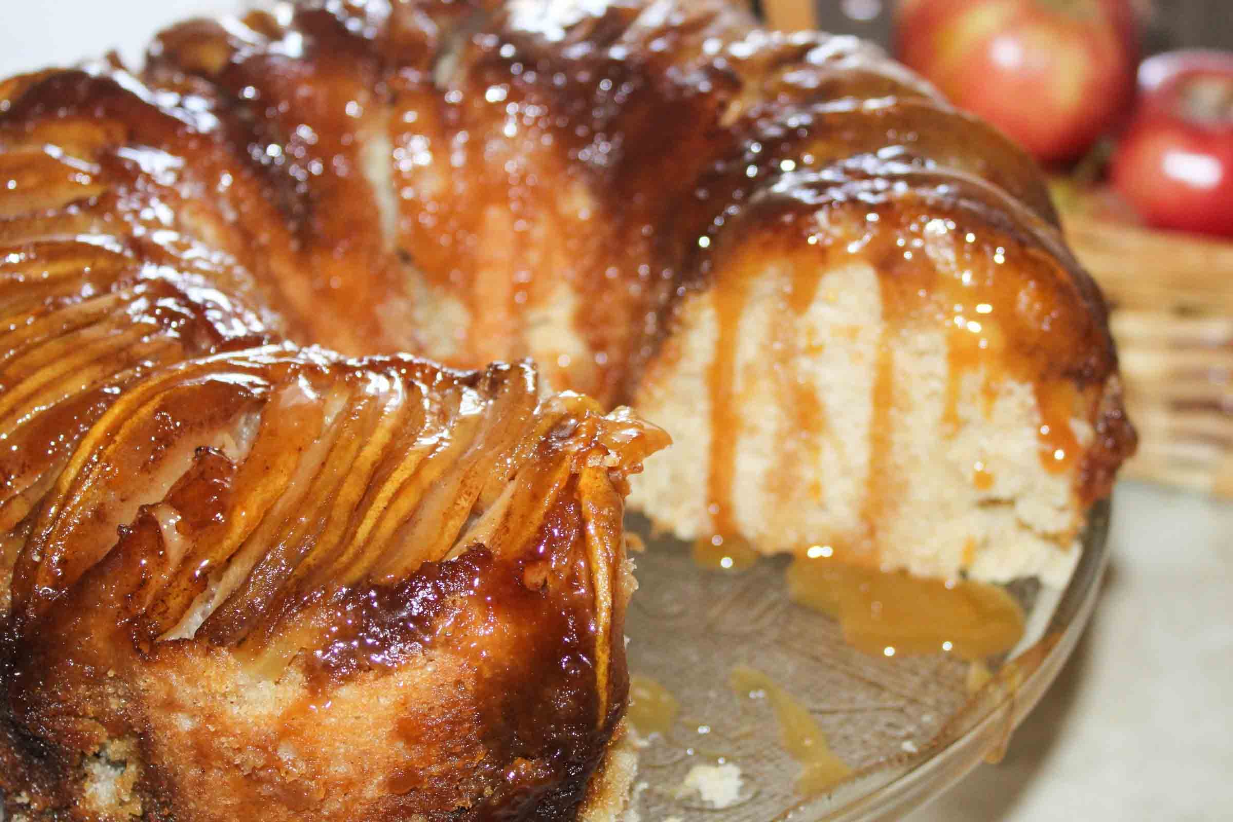 Apple upside down bundt cake with a slice removed and caramel sauce dripping down the sides.