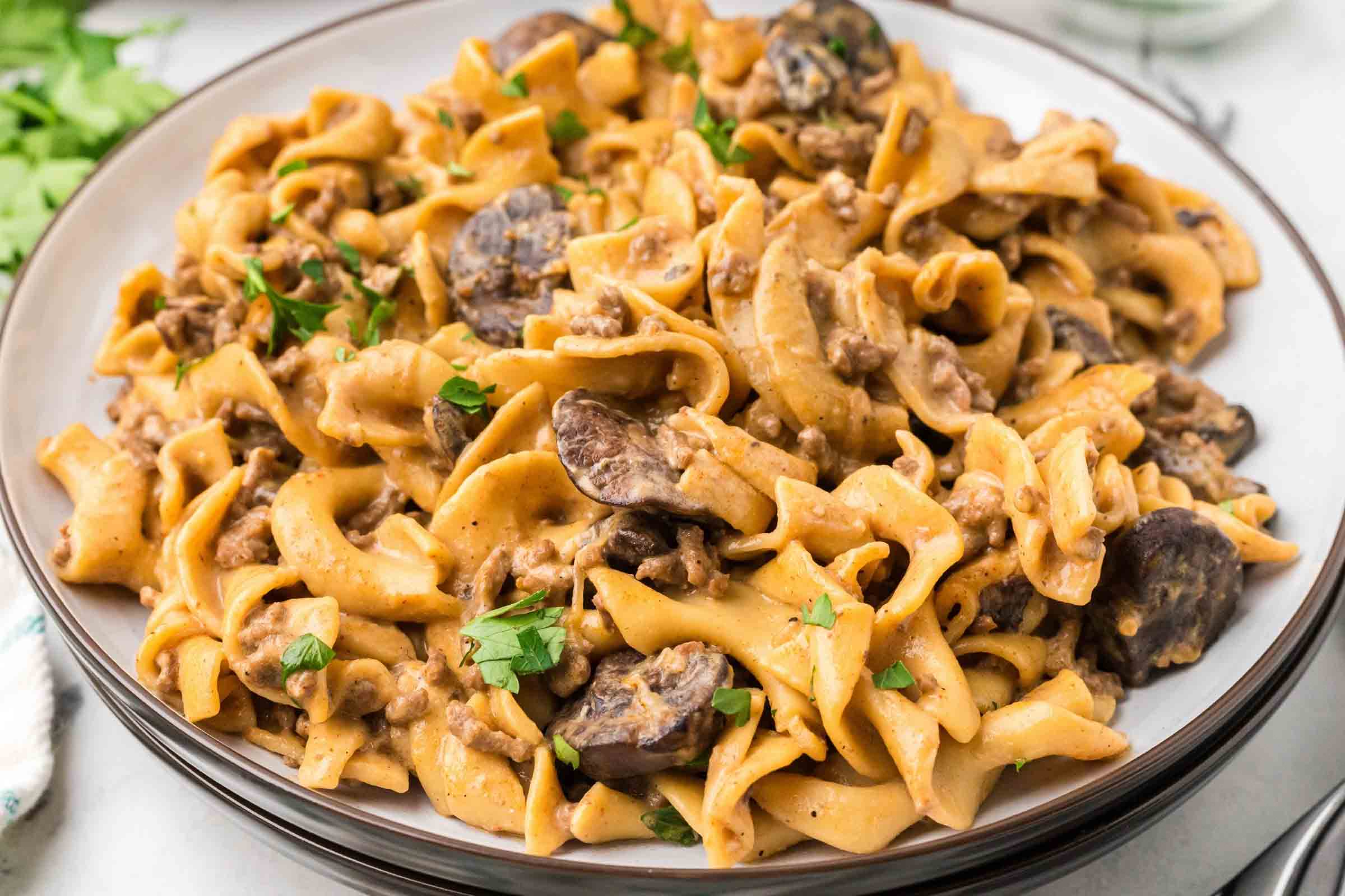 A plate with egg noodles, sliced mushrooms, and ground beef in a sauce garnished with chopped parsley.