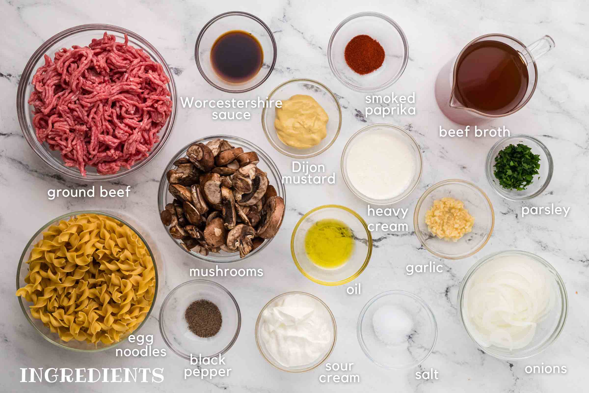 Labeled photo of ingredients: ground bee, egg noodles, mushrooms, dijon mustard, smoked paprika, beef broth, heavy cream, minced garlic, parsley, onions, sour cream, oil, salt, and pepper.