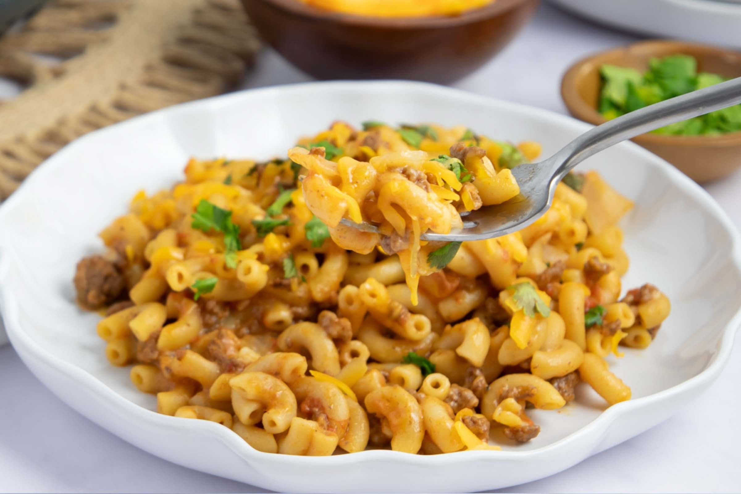 Plate of cheesy elbow macaroni and ground beef in seasoned tomatoes garnished with cilantro.