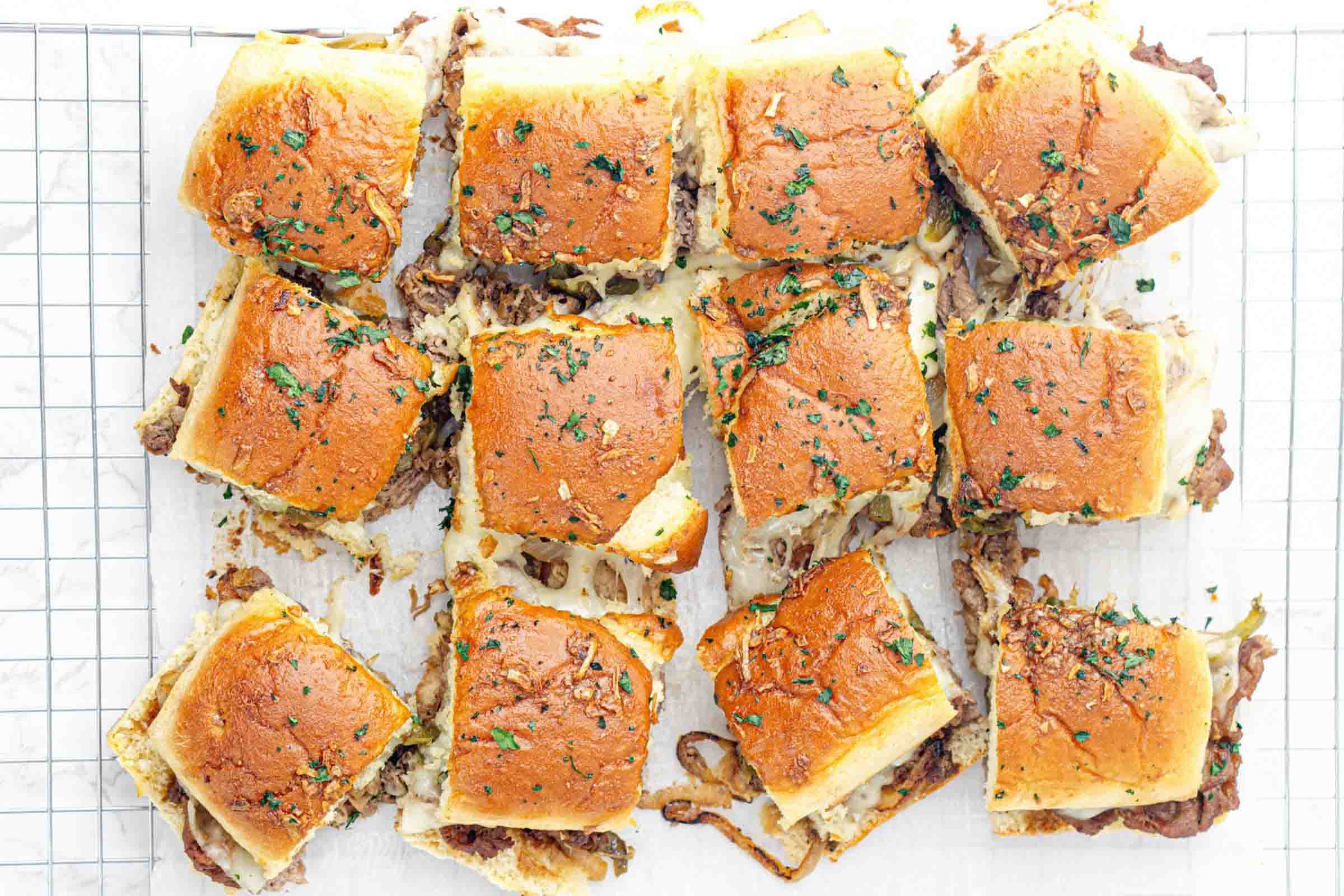 Philly cheesesteak sliders on parchment paper after baking.