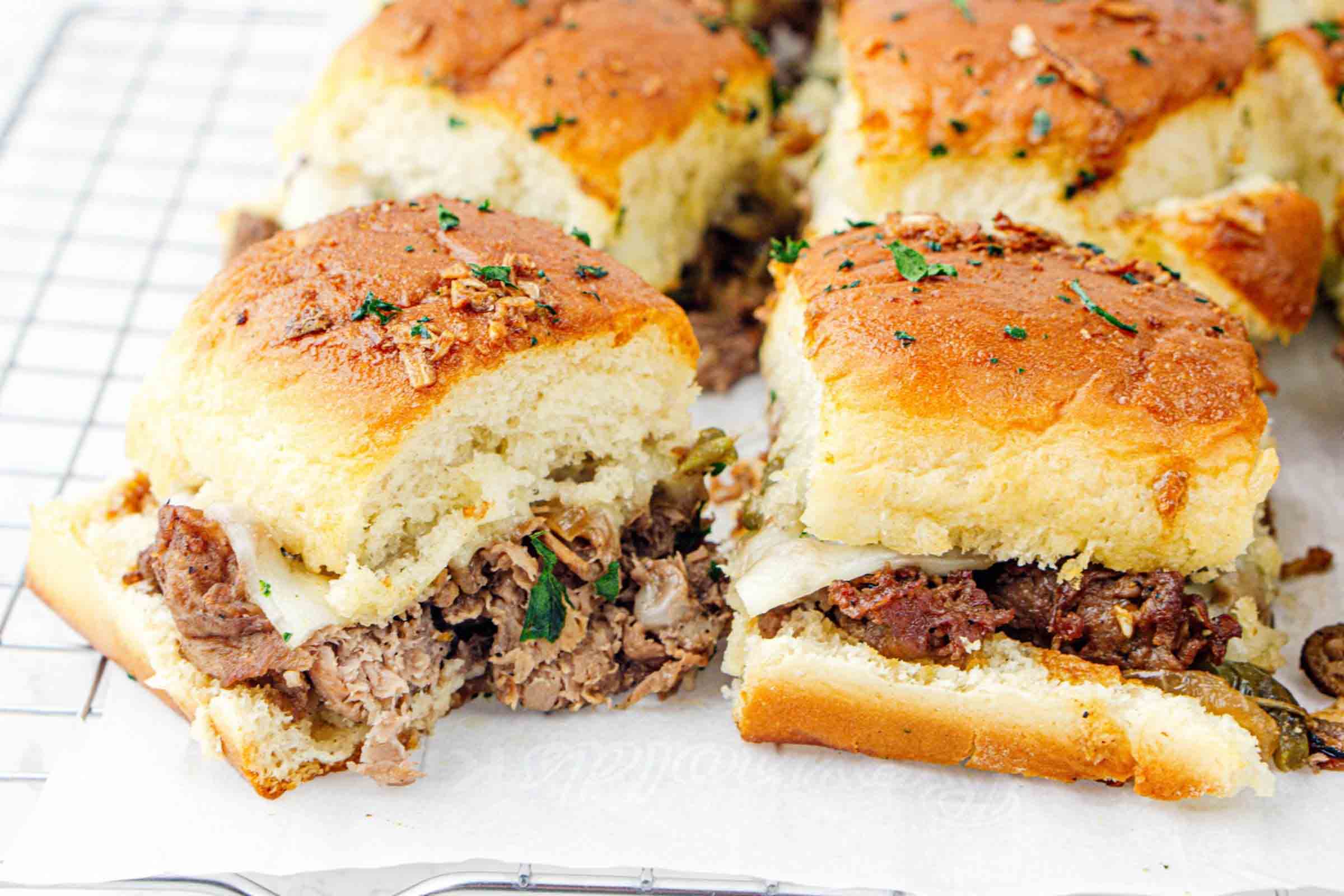 Philly cheesesteak sliders on parchment paper after baking.