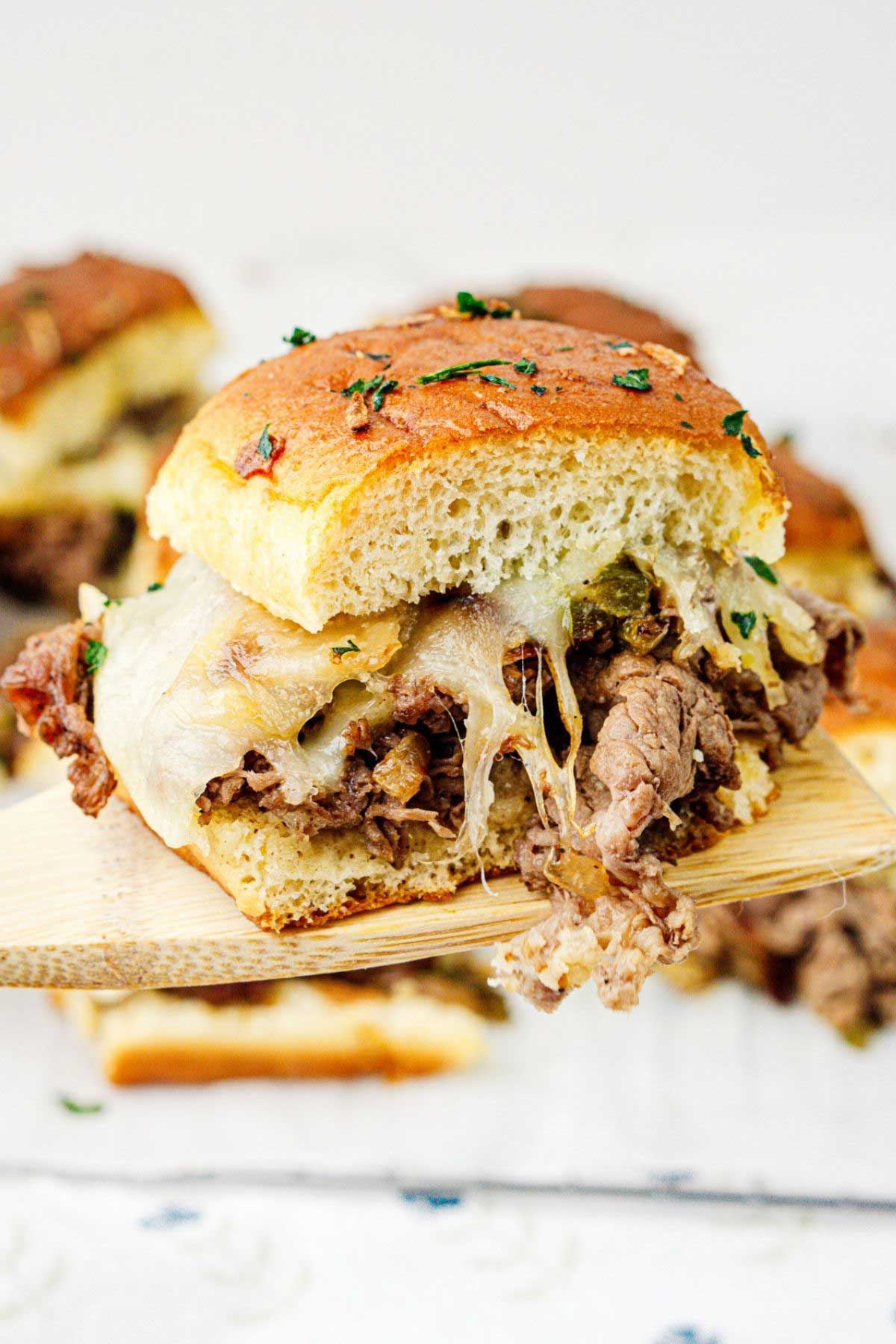 Philly cheesesteak slider on a wooden spatula raised to the camera.