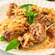 A plate of meatballs in a creamy red sauce with orzo with a meatball cut open on a fork.