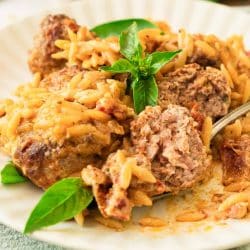 A plate of meatballs in a creamy red sauce with orzo with a meatball cut open on a fork.