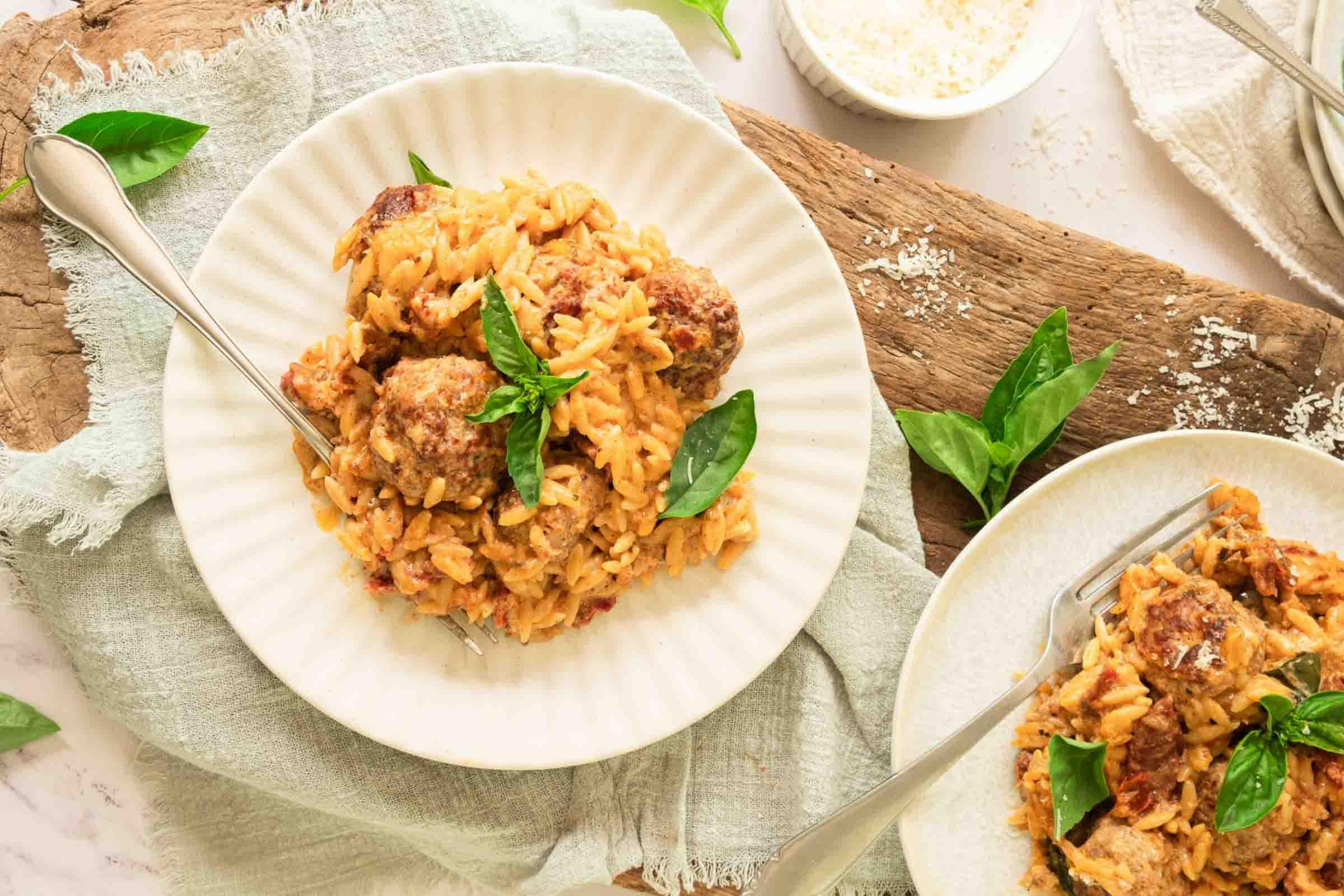 Plates of meatballs with orzo in a creamy sun-dried tomato sauce and garnished with fresh basil.