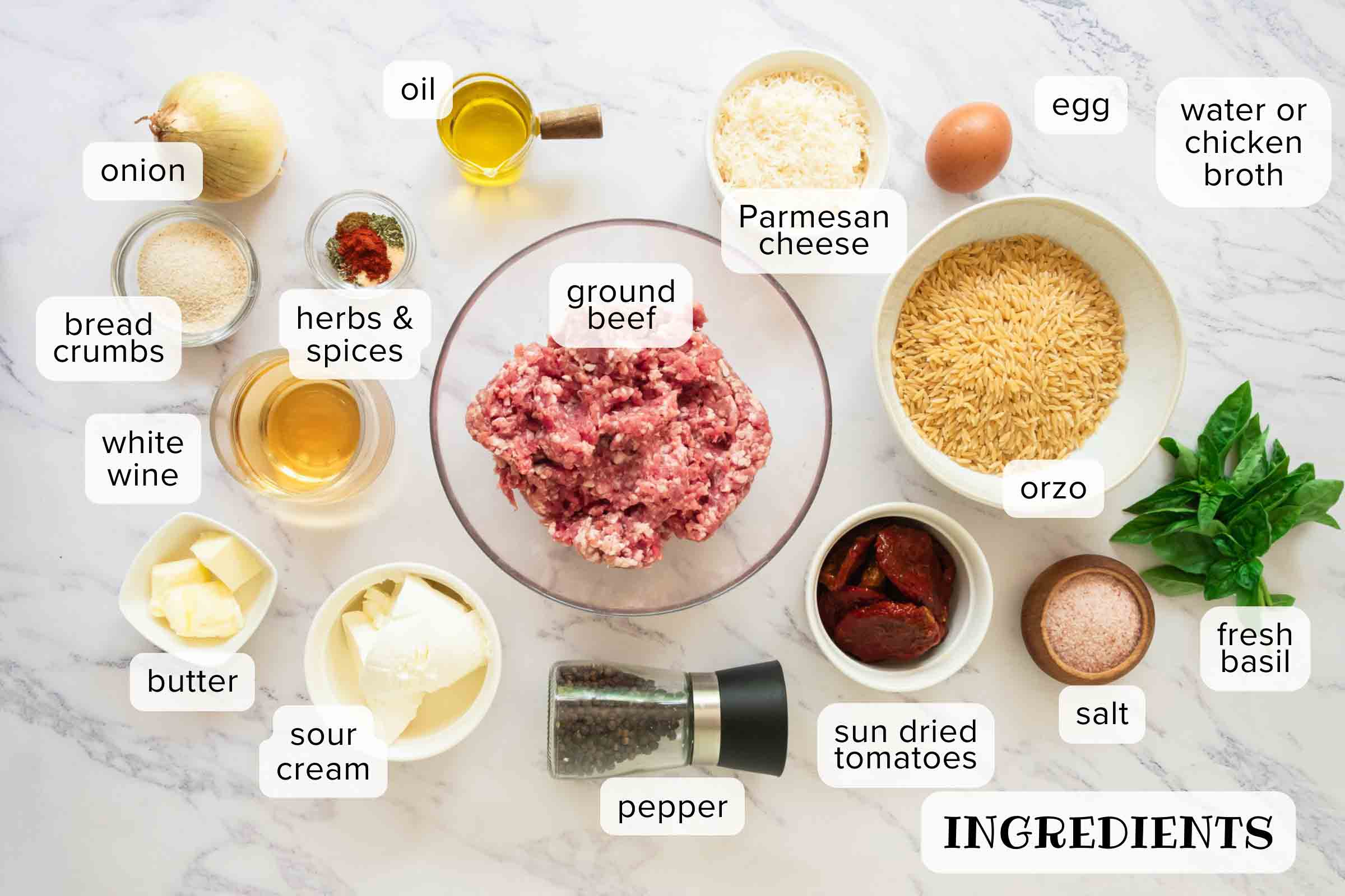 Labeled ingredients for Tuscan meatballs with orzo: onion, bread crumbs, herbs & spices, white wine, butter, sour cream, pepper, sun-dried tomatoes, salt, fresh basil, orzo, egg, ground beef, Parmesan cheese, oil, and water or chicken broth.